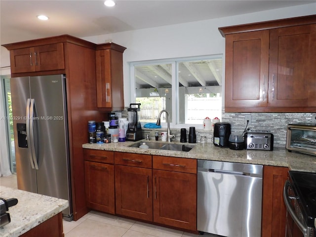 kitchen featuring appliances with stainless steel finishes, a sink, light stone counters, light tile patterned flooring, and backsplash