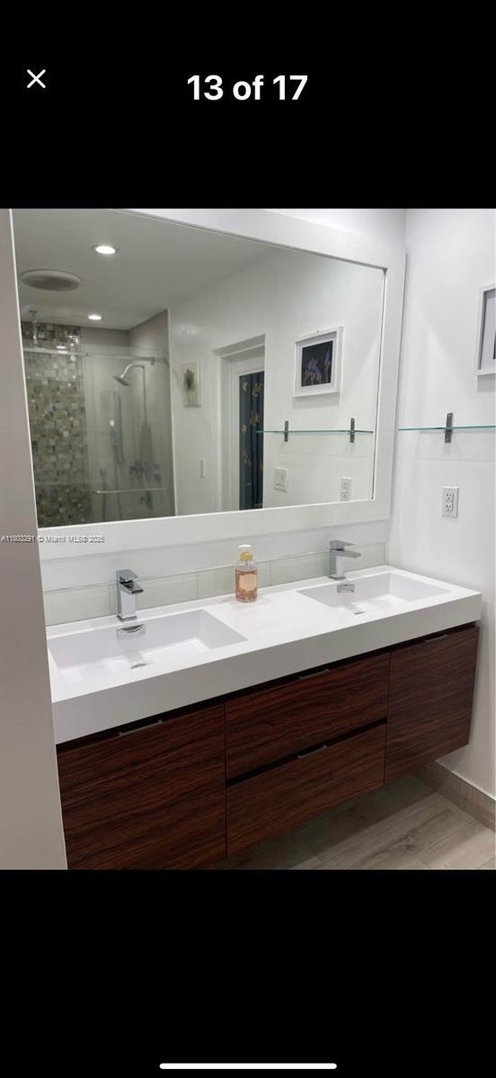 full bath with a shower stall, double vanity, and wood finished floors