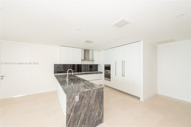 700 NE 26th Ter Unit 903, Miami, FL 33137 - kitchen featuring wall chimney exhaust hood, a peninsula, dark stone counters, white cabinets, and stainless steel double oven