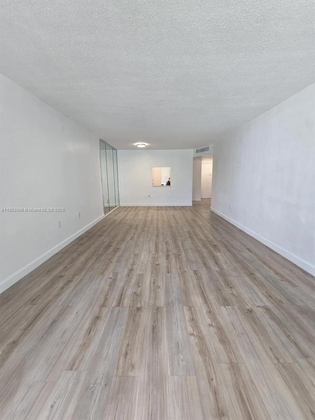 1201 NE 191st St Unit G211, Miami, FL 33179 - unfurnished living room featuring a textured ceiling, light wood-style flooring, and baseboards
