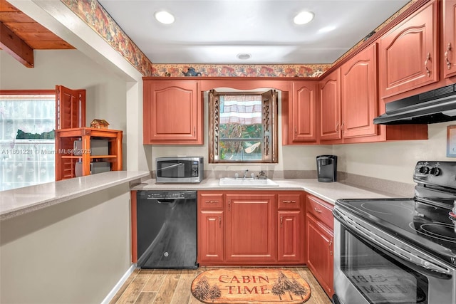 kitchen featuring stainless steel appliances, a sink, under cabinet range hood, light countertops, and light wood-style floors