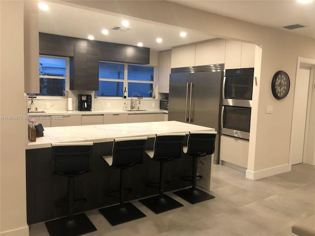 9224 Byron Ave, Surfside, FL 33154 - kitchen featuring a sink, a breakfast bar area, appliances with stainless steel finishes, light stone counters, and recessed lighting