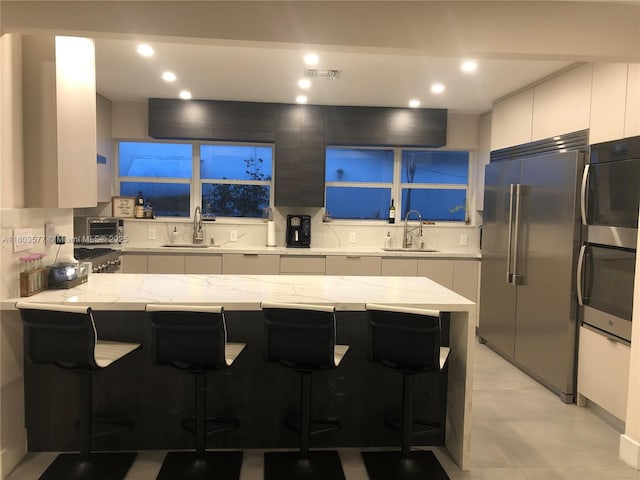 9224 Byron Ave, Surfside, FL 33154 - kitchen featuring high end fridge, a sink, a kitchen breakfast bar, light stone counters, and recessed lighting