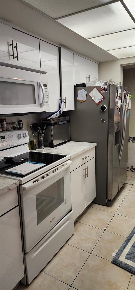 kitchen featuring white appliances, white cabinets, light tile patterned floors, and light countertops