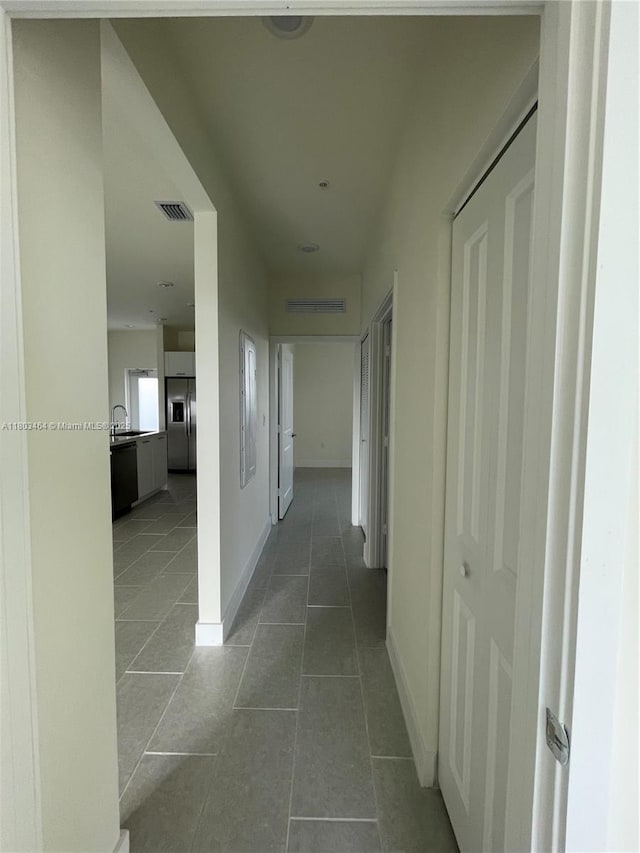 corridor featuring tile patterned flooring, a sink, and baseboards