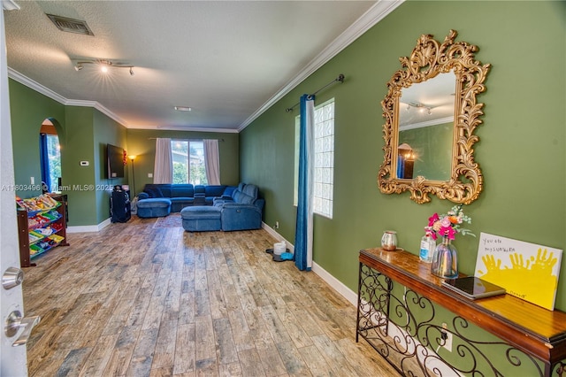living room with arched walkways, wood finished floors, crown molding, baseboards, and a textured ceiling