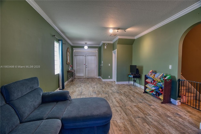 living area featuring arched walkways, wood finished floors, baseboards, a textured ceiling, and ornamental molding