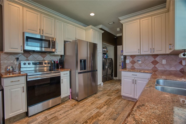 kitchen with appliances with stainless steel finishes, separate washer and dryer, crown molding, light wood-type flooring, and backsplash