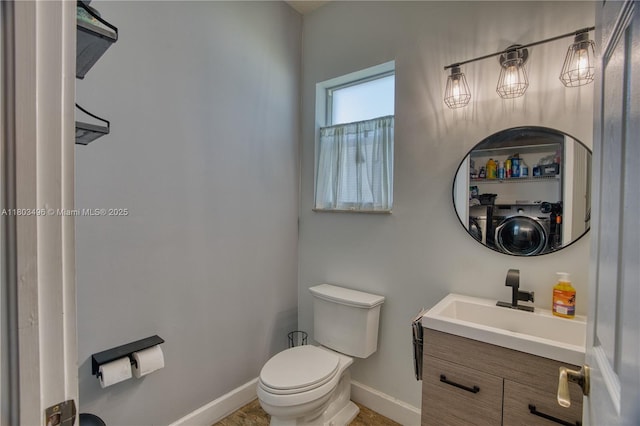 bathroom with toilet, baseboards, vanity, and washer / dryer