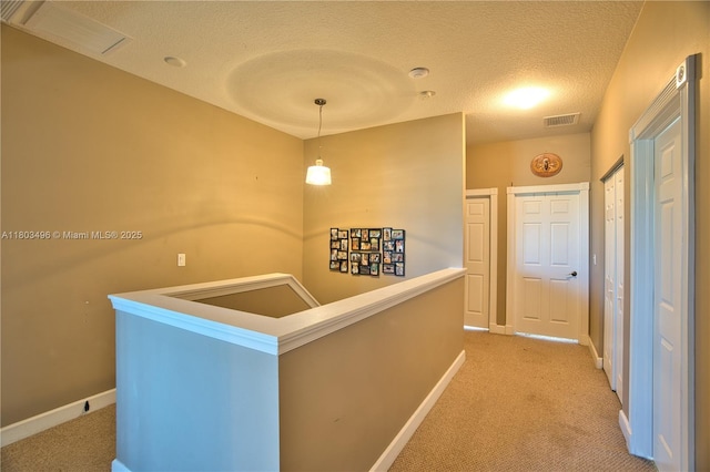 corridor featuring an upstairs landing, light colored carpet, a textured ceiling, and baseboards