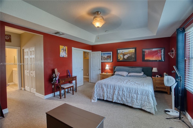 bedroom with carpet flooring, a tray ceiling, baseboards, and ensuite bathroom
