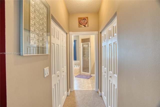 hall with light colored carpet, a textured ceiling, and baseboards