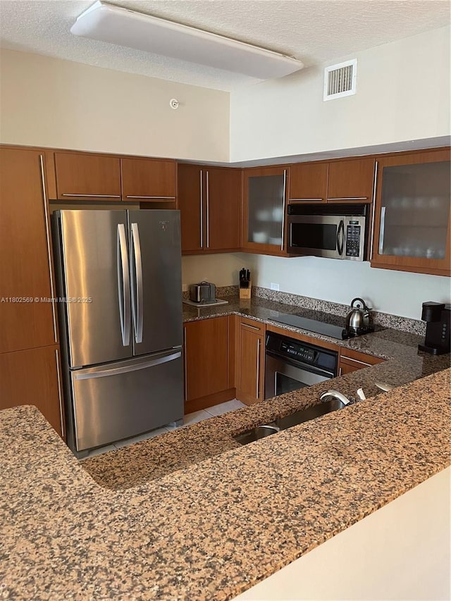 2080 S Ocean Dr Unit Ph4, Hallandale Beach, FL 33009 - kitchen featuring stainless steel appliances, brown cabinets, dark stone counters, glass insert cabinets, and a textured ceiling