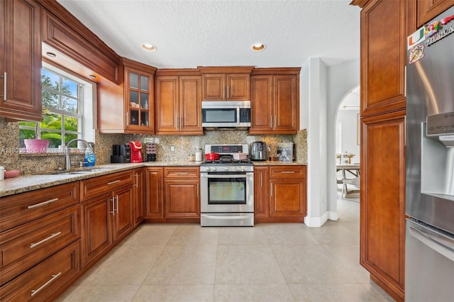 2238 NW 139th Ave, Sunrise, FL 33323 - kitchen featuring appliances with stainless steel finishes, a sink, arched walkways, decorative backsplash, and light stone counters