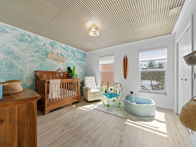 7165 W 13th Ave, Hialeah, FL 33014 - bedroom featuring wallpapered walls, a crib, an accent wall, and wood finished floors