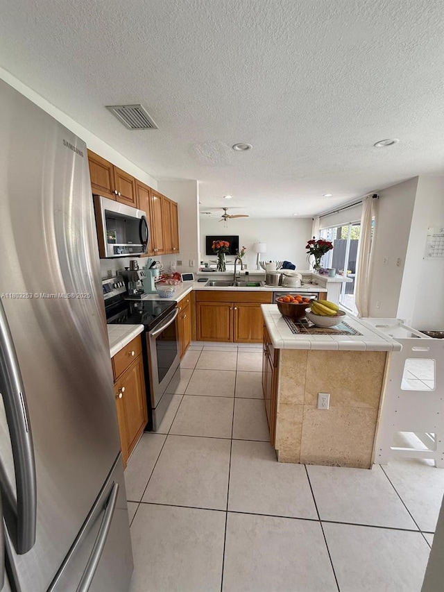9740 SW 155th Ave, Miami, FL 33196 - kitchen with stainless steel appliances, a peninsula, a sink, brown cabinetry, and tile countertops