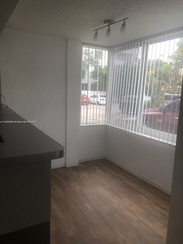 250 180th Dr Unit 108, Sunny Isles Beach, FL 33160 - unfurnished dining area featuring rail lighting, healthy amount of natural light, wood finished floors, baseboards, and a textured ceiling