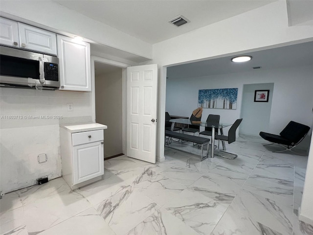 1472 NE 150th St, Miami, FL 33161 - kitchen with stainless steel microwave, white cabinetry, light countertops, and light marble finish floors