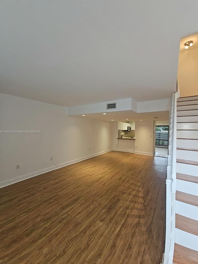 unfurnished living room with wood finished floors, baseboards, and stairway