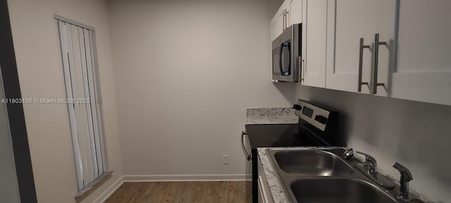 kitchen featuring stainless steel appliances, a sink, white cabinetry, wood finished floors, and baseboards