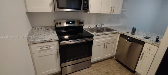 kitchen with appliances with stainless steel finishes, a sink, white cabinets, and light wood-style flooring