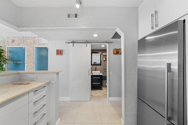 1228 W Ave Unit 704, Miami Beach, FL 33139 - kitchen featuring stainless steel refrigerator, white cabinetry, light tile patterned flooring, a barn door, and light stone countertops