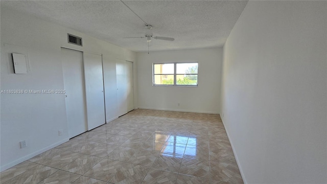 unfurnished bedroom featuring two closets, a textured ceiling, ceiling fan, baseboards, and light marble finish flooring