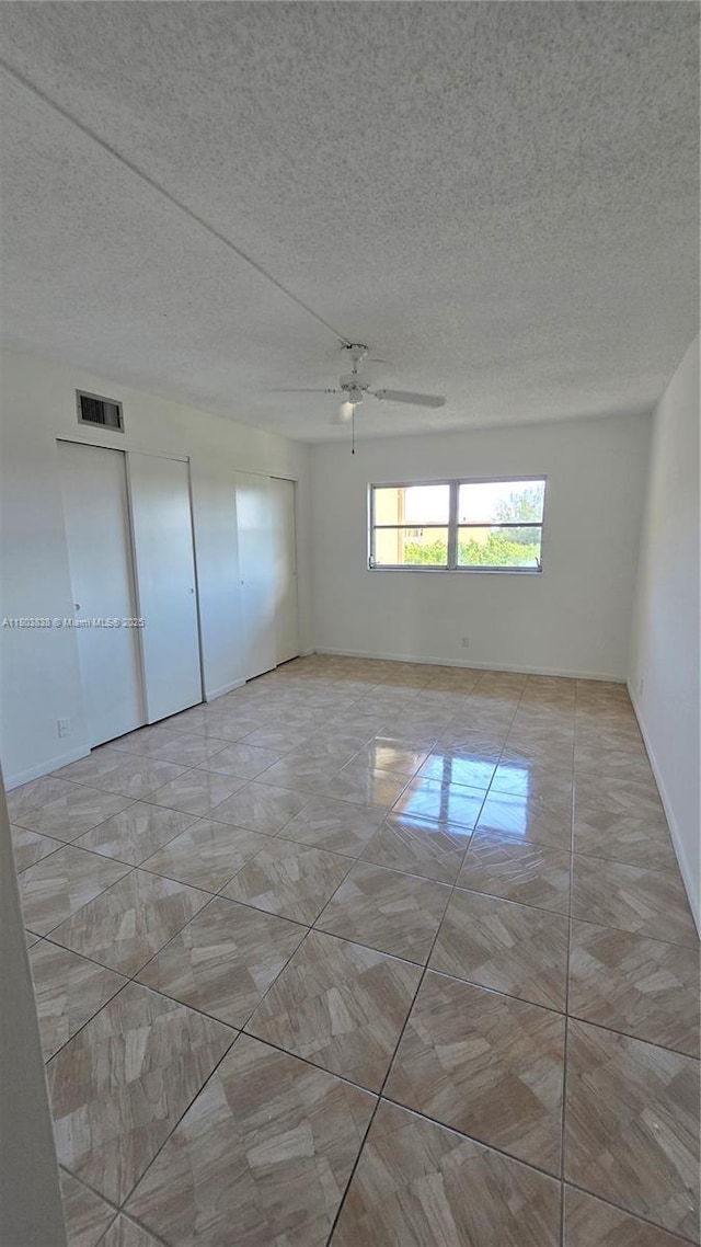unfurnished room with ceiling fan, marble finish floors, a textured ceiling, and baseboards