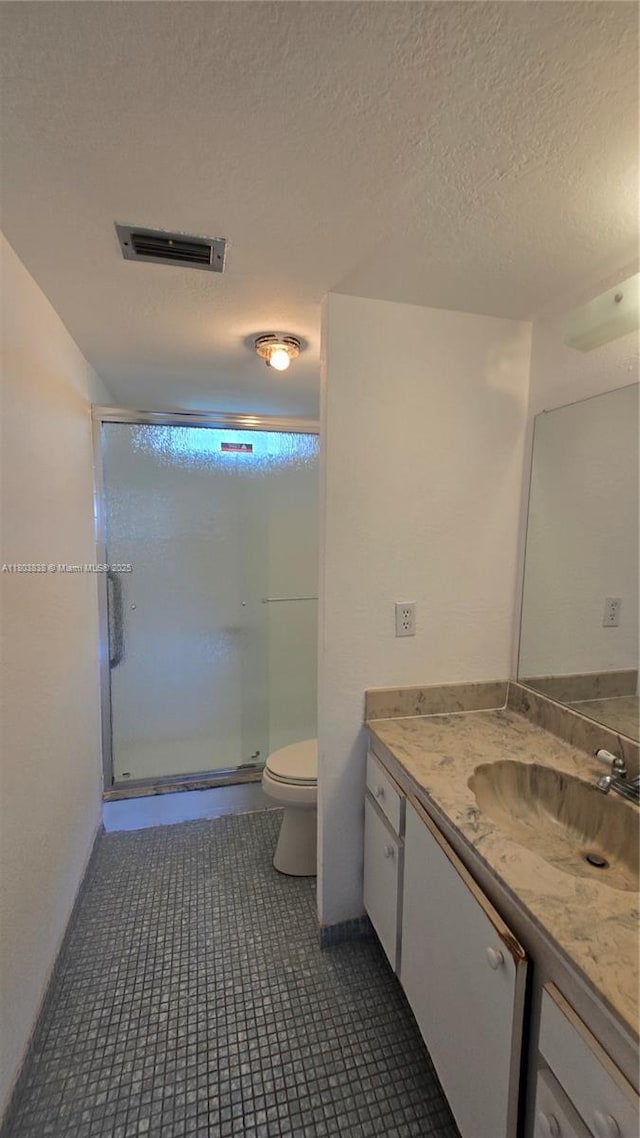 full bath featuring a stall shower, toilet, vanity, a textured ceiling, and tile patterned floors