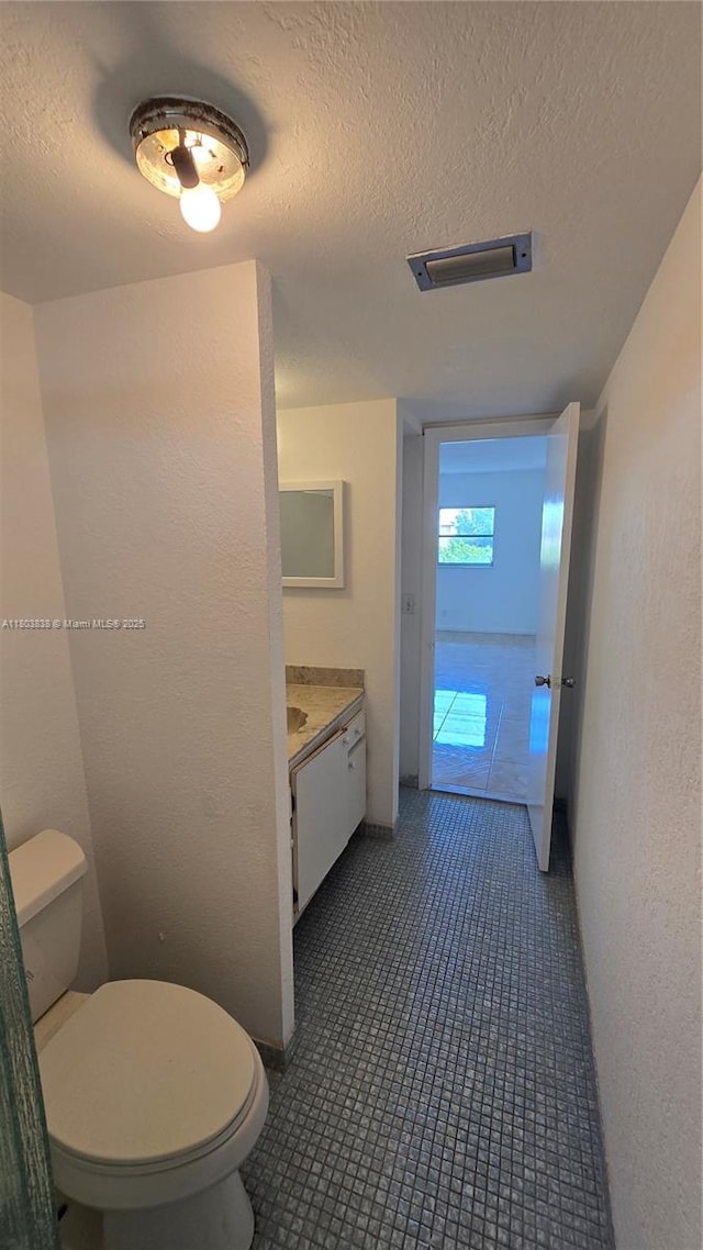 bathroom with toilet, a textured ceiling, vanity, and tile patterned flooring