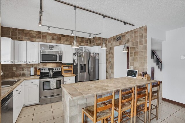 16465 NE 26th Ave Unit 18, North Miami Beach, FL 33160 - kitchen with stainless steel appliances, track lighting, tile countertops, white cabinets, and a textured ceiling