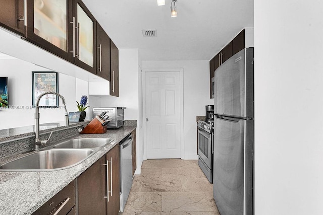 kitchen with appliances with stainless steel finishes, a sink, light marble finish flooring, and dark brown cabinetry