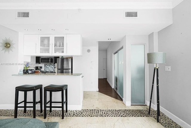 275 NE 18th St Unit 306, Miami, FL 33132 - kitchen featuring stainless steel appliances, white cabinetry, a kitchen bar, glass insert cabinets, and light stone counters