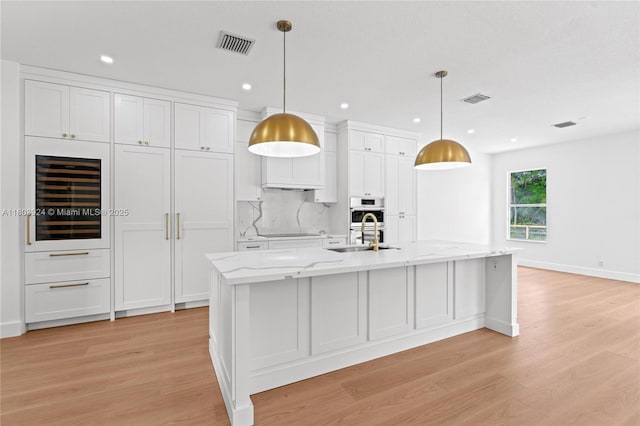 kitchen with a sink, wine cooler, light wood finished floors, white cabinets, and a spacious island
