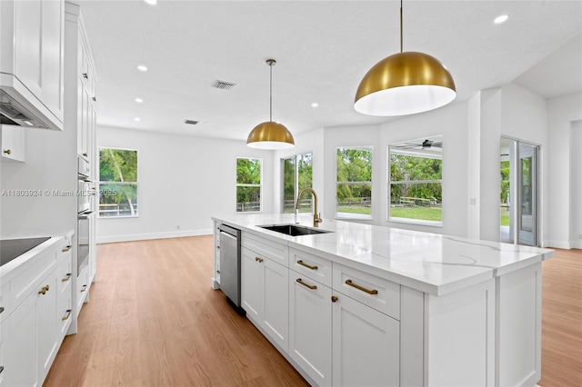 kitchen featuring a sink, light wood finished floors, recessed lighting, white cabinets, and a center island with sink