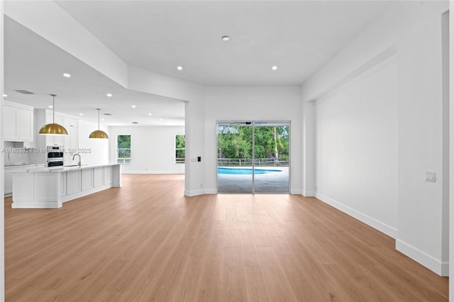 unfurnished living room featuring recessed lighting, plenty of natural light, light wood-style flooring, baseboards, and a sink