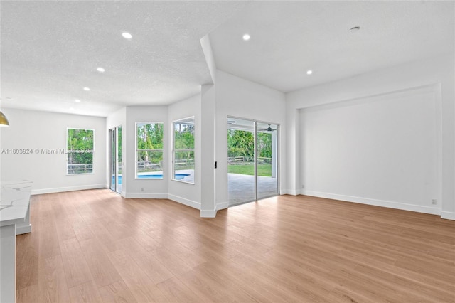 unfurnished living room featuring recessed lighting, baseboards, light wood finished floors, and a textured ceiling
