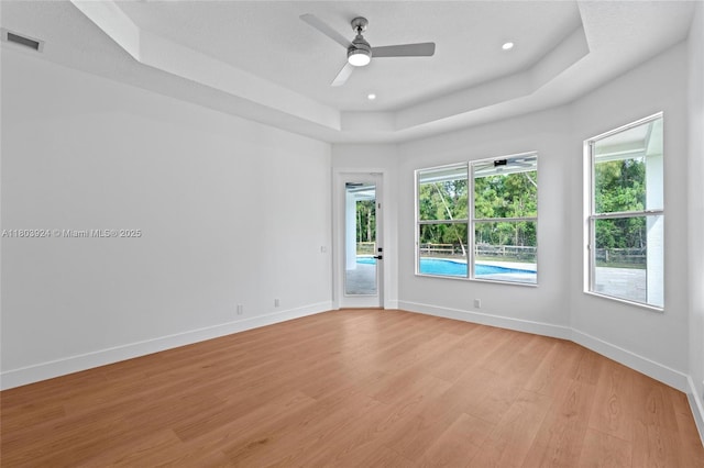 unfurnished room with a tray ceiling, light wood-style floors, ceiling fan, baseboards, and recessed lighting