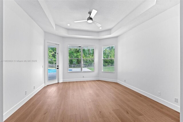 unfurnished room featuring light wood finished floors, a tray ceiling, a ceiling fan, baseboards, and a textured ceiling