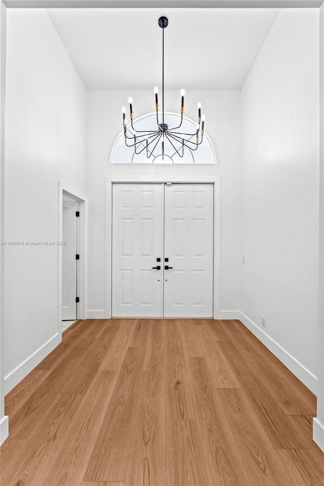 entrance foyer with a chandelier, light wood-style flooring, and baseboards