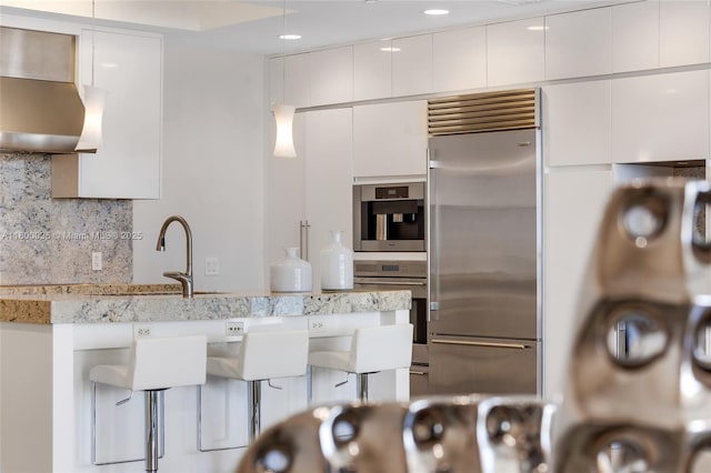 9705 Collins Ave Unit 1805N, Bal Harbour, FL 33154 - kitchen with appliances with stainless steel finishes, wall chimney exhaust hood, a sink, a breakfast bar area, and backsplash