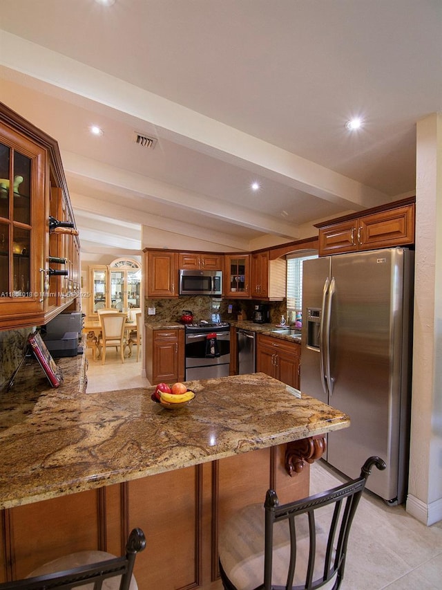 10715 SW 139th Ct, Miami, FL 33186 - kitchen with appliances with stainless steel finishes, a peninsula, light stone counters, brown cabinetry, and decorative backsplash