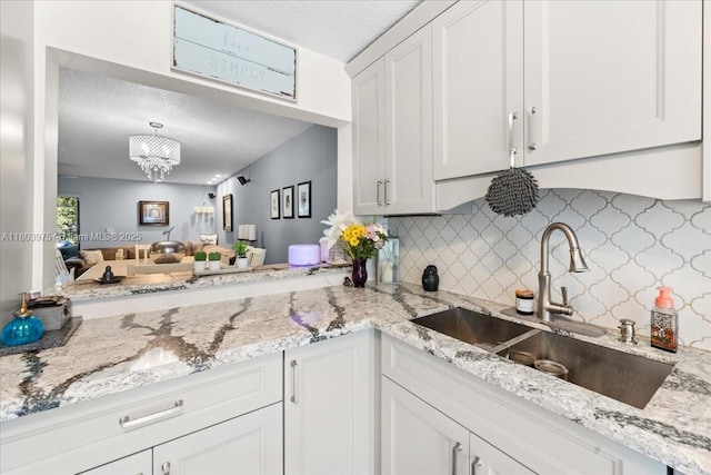 1150 NW 99th Ave Unit 69, Pembroke Pines, FL 33024 - kitchen featuring a sink, a textured ceiling, white cabinets, backsplash, and light stone counters