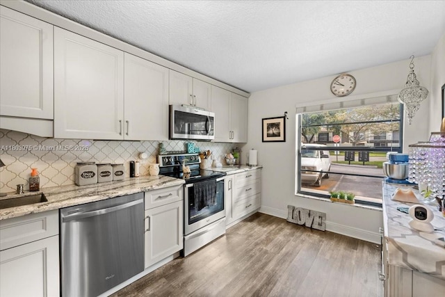 1150 NW 99th Ave Unit 69, Pembroke Pines, FL 33024 - kitchen featuring stainless steel appliances, wood finished floors, decorative backsplash, baseboards, and a textured ceiling