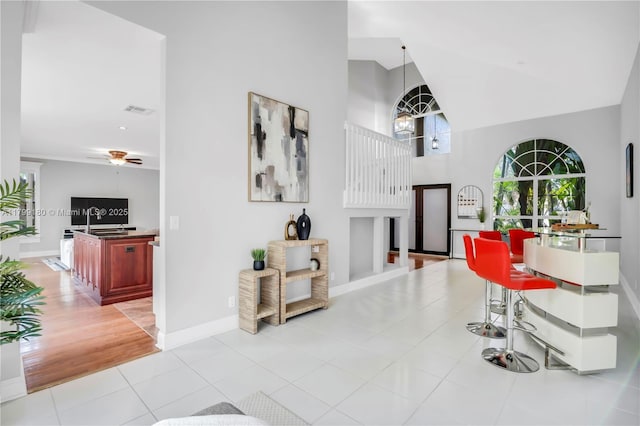 living area with a high ceiling, ceiling fan, baseboards, and light tile patterned floors