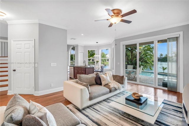 living area featuring light wood-style floors, a ceiling fan, crown molding, baseboards, and recessed lighting