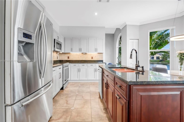 kitchen featuring appliances with stainless steel finishes, a sink, tasteful backsplash, white cabinets, and dark stone counters