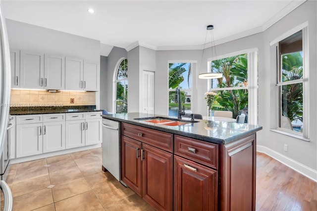kitchen featuring dishwasher, a sink, backsplash, dark stone counters, and white cabinetry