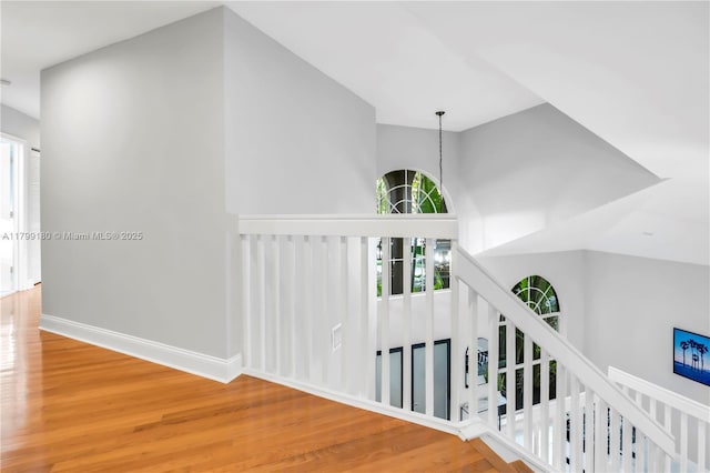 hall with wood finished floors, baseboards, and an upstairs landing