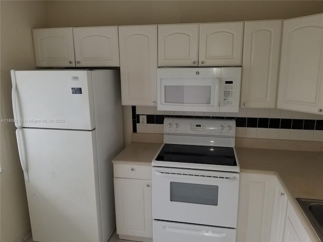 kitchen with white appliances, backsplash, white cabinetry, light countertops, and a sink